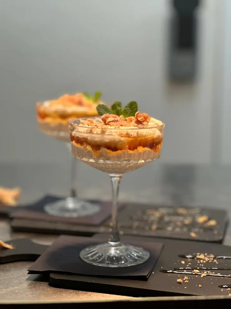 Zwei Gläser mit geschichtetem Dessert aus Creme, Karamell und Keksstreuseln