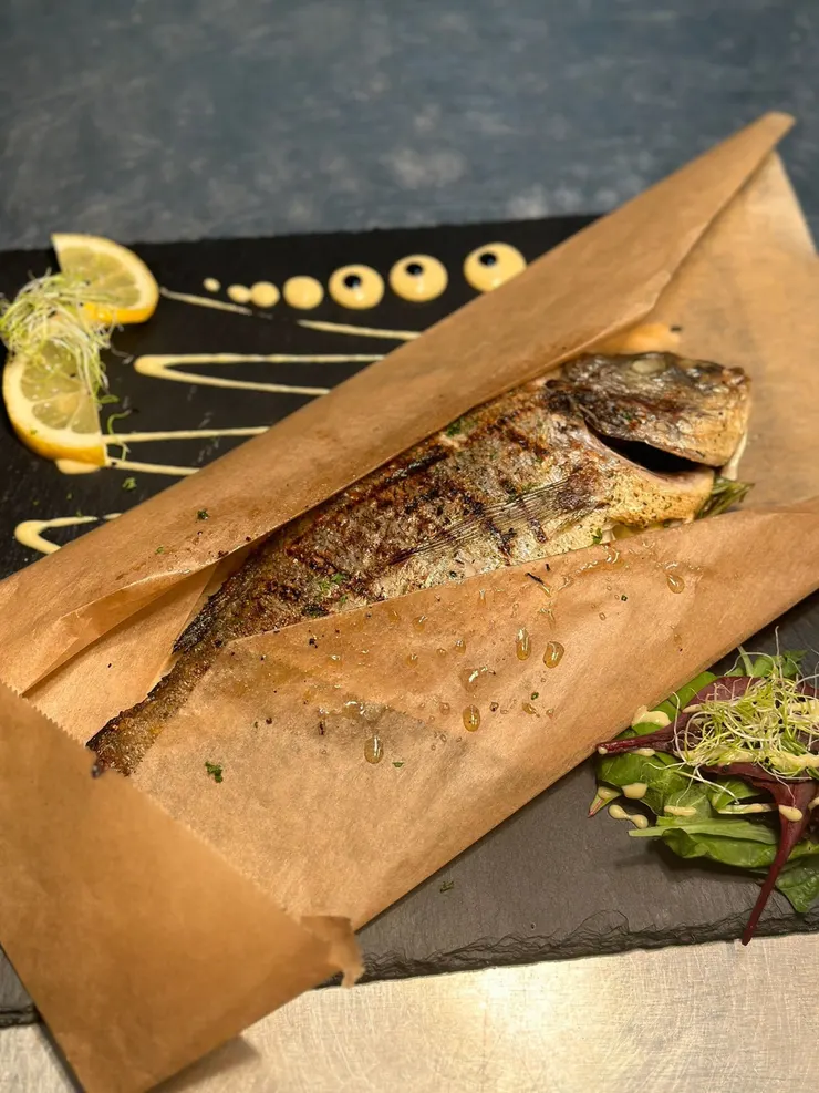 Gegrillter ganzer Fisch in Pergamentpapier mit Zitronenscheiben