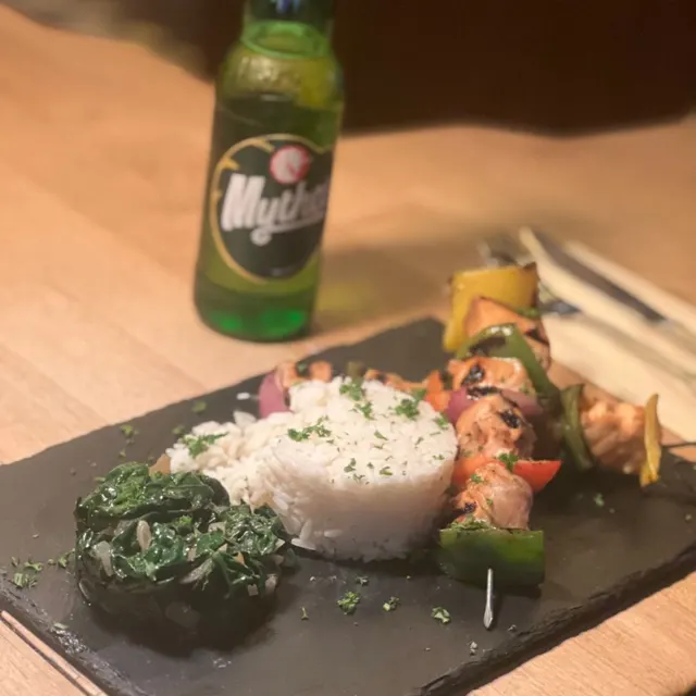 Grillspieße mit Reis und Spinat, dahinter eine Flasche Mythos-Bier
