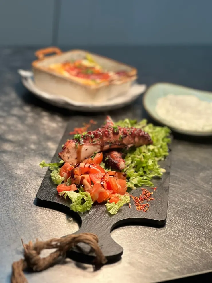 Gegrillter Oktopus auf einem Holzbrett mit Tomatensalat